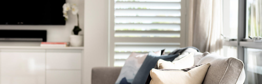 Cozy living room featuring aluminium shutters, soft cushions, and a modern TV setup.