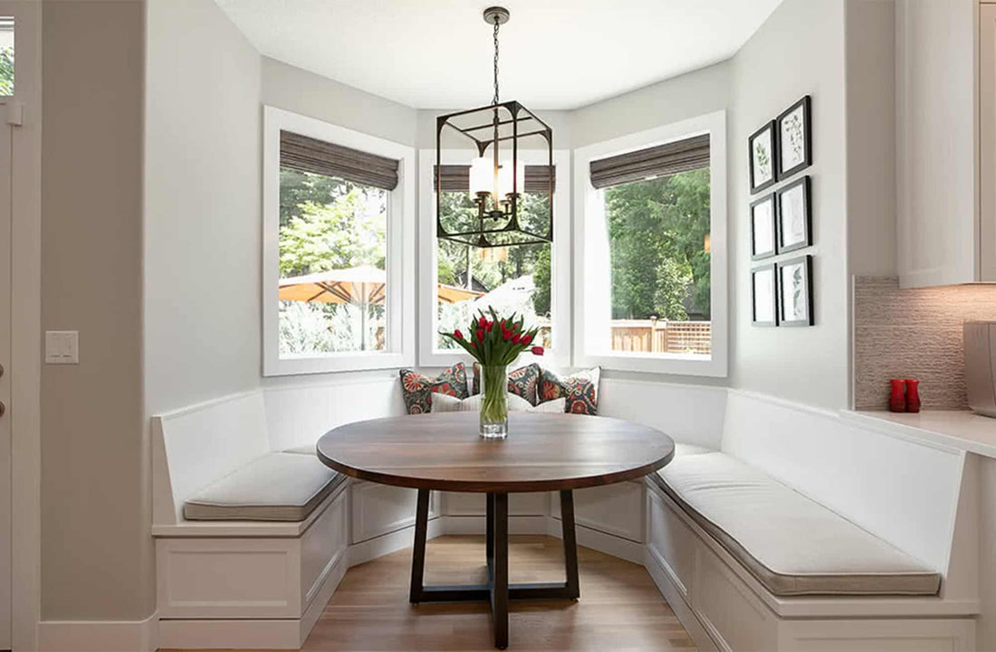 Cozy bay window seat with a round table, elegant lighting, and flower vase, perfect for relaxation.