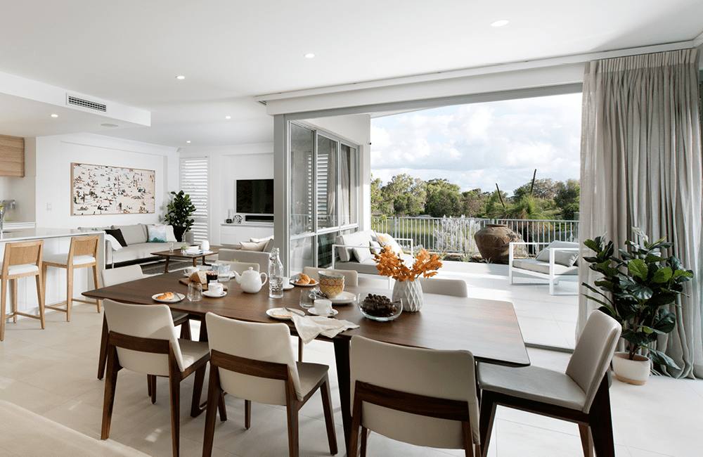 Modern dining area with a wooden table, stylish chairs, and large windows opening to a scenic outdoor view.