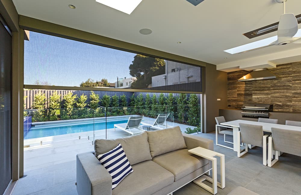 Modern outdoor blinds providing shade for an entertaining area overlooking a pool and garden.