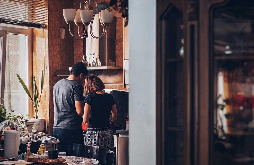 Couple cooking together in a warm, inviting kitchen, preparing for house guests with a cozy atmosphere.