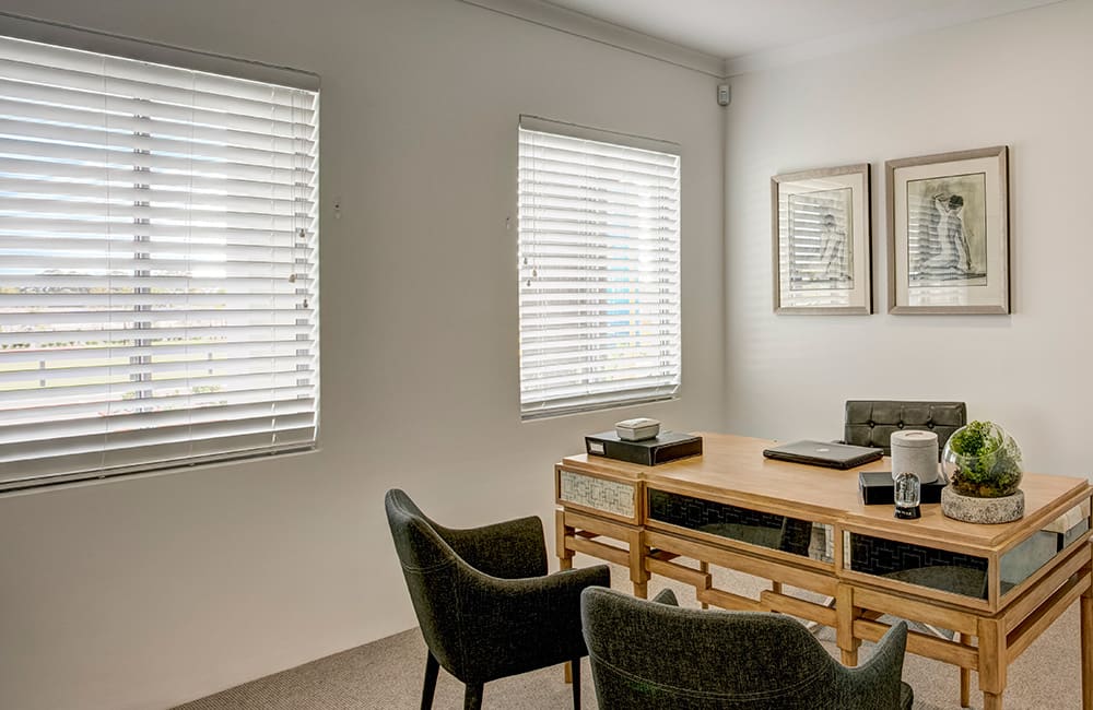 Modern office with white window blinds, a wooden desk, and stylish chairs creating a bright workspace.
