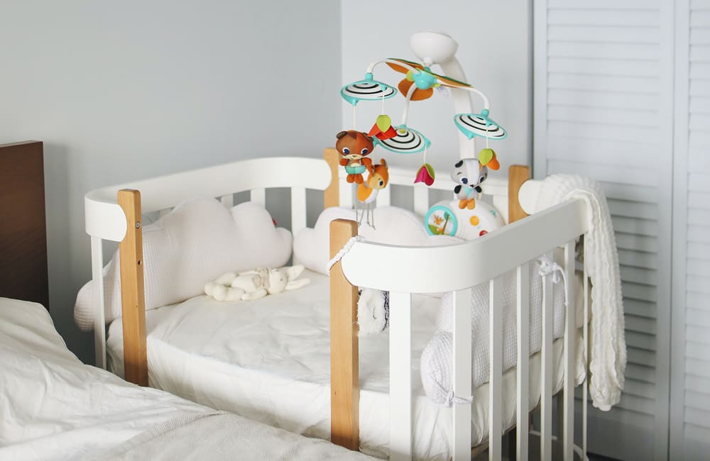 Cozy nursery crib with soft bedding and colorful mobile, perfect for a baby's safe sleep environment.