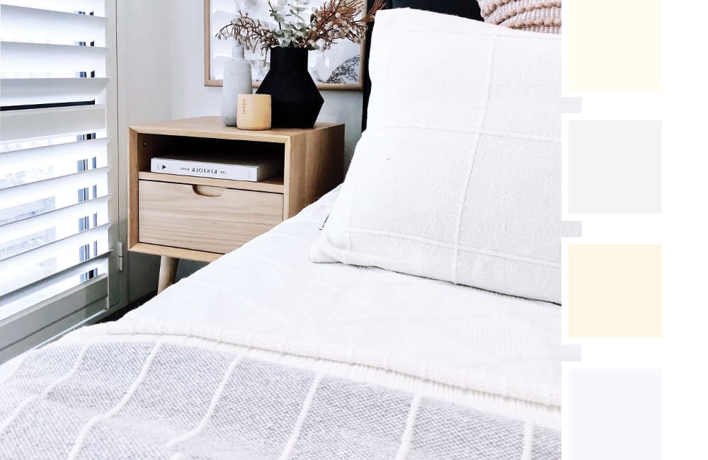 A cozy bedroom featuring white bedding, wooden nightstand, and a color palette of popular paint shades for matching blinds.
