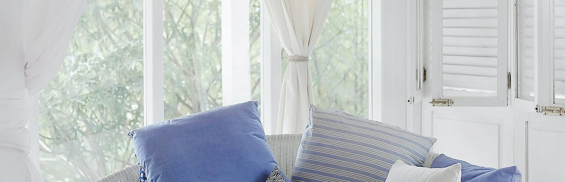 Cozy indoor seating area with blue and white pillows, bright curtains, and natural light filtering through the windows.