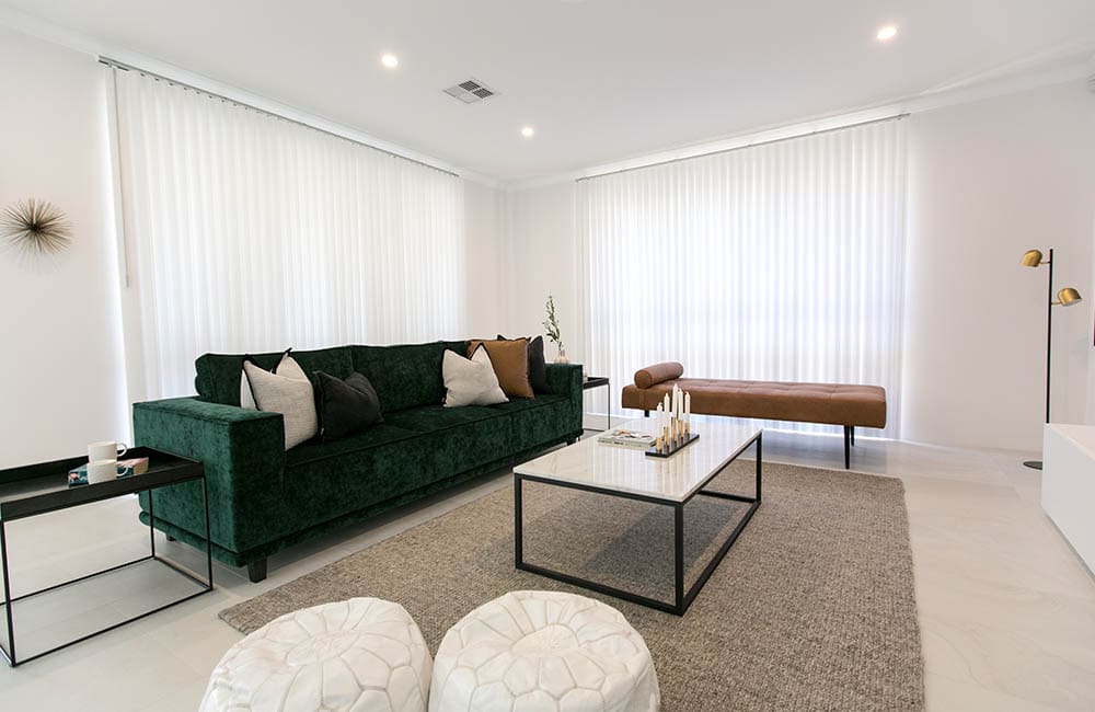 Stylish living room featuring green velvet couch, patterned cushions, and elegant blinds for a bohemian vibe.