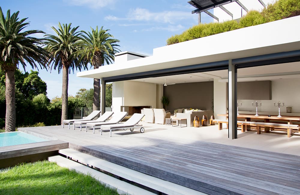 Modern alfresco kitchen design featuring outdoor seating and pool surrounded by palm trees.