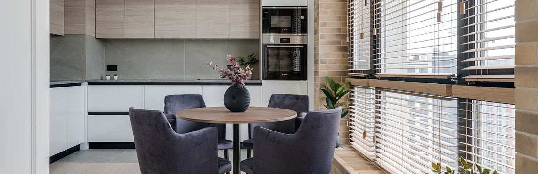 Modern kitchen featuring Venetian blinds on windows, a round dining table, and stylish upholstered chairs.