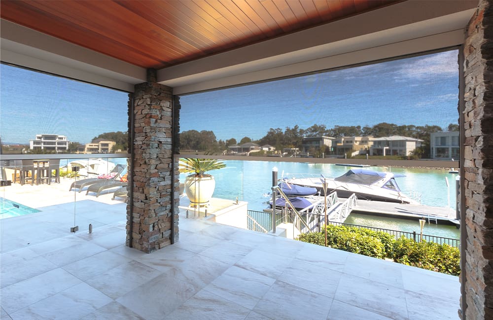 Modern patio view overlooking a tranquil waterway with boats, featuring stone pillars and elegant outdoor furniture.
