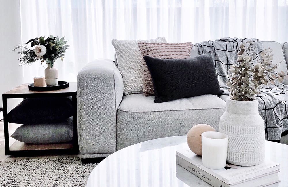 Modern living room with gray couch, decorative pillows, stylish side table, and fresh flowers for a chic interior design.