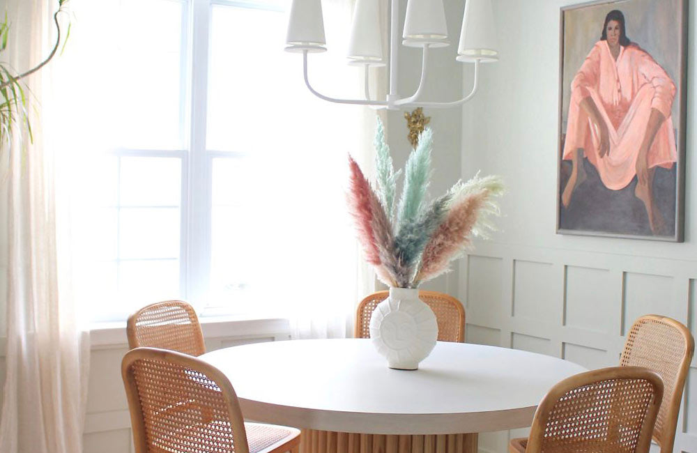 Stylish dining area featuring a round table, chic chairs, and a vase of decorative dried flowers.