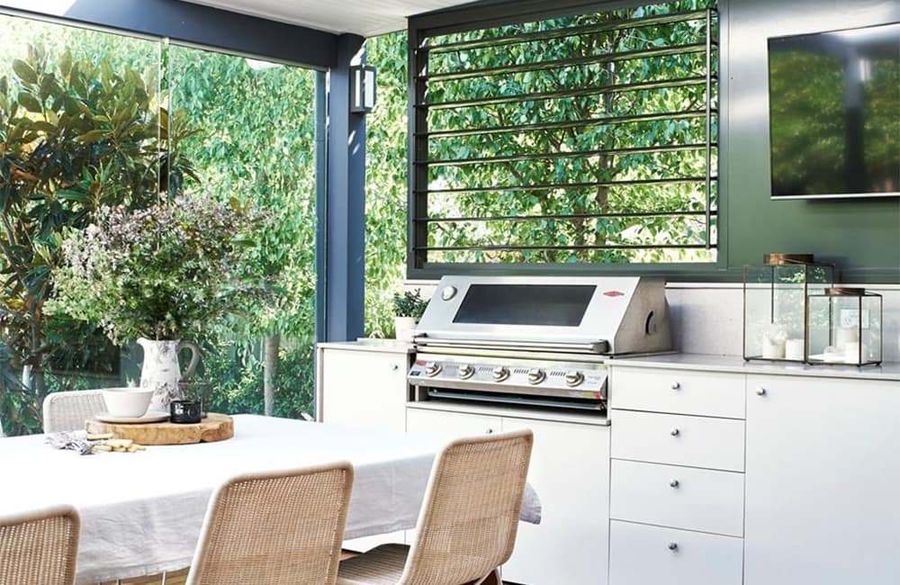 Modern outdoor kitchen with a grill, dining table, and greenery, perfect for entertaining and relaxation.