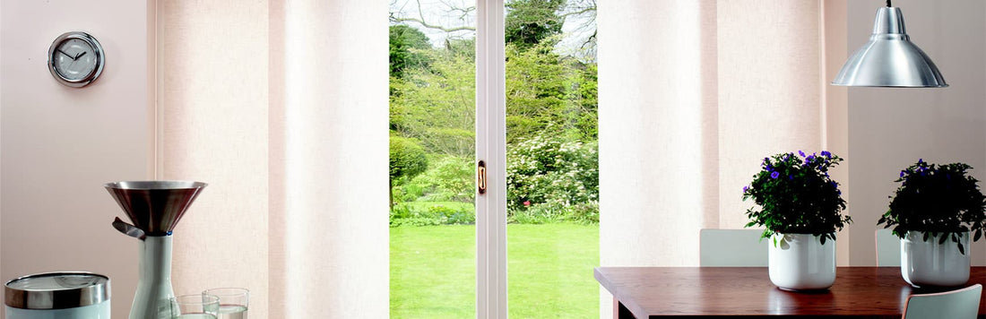 Cozy dining area with Panel Glide blinds covering a door leading to a green backyard garden.