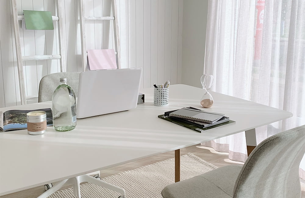 Minimalist office desk with laptop, water bottle, notebooks, and natural light filtering through curtains.